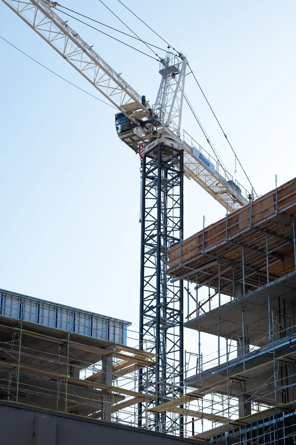 Tower crane beside a mid-rise building under construction against a blue sky